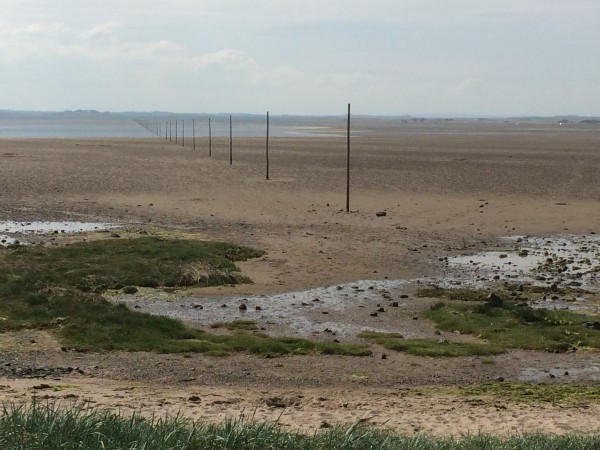 In the distance, towards the mainland, the tide is already moving in towards the Pilgrim's Way marker posts.